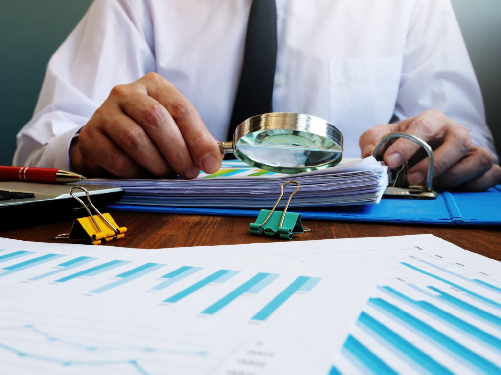 A professional scrutinizes financial documents with a magnifying glass.