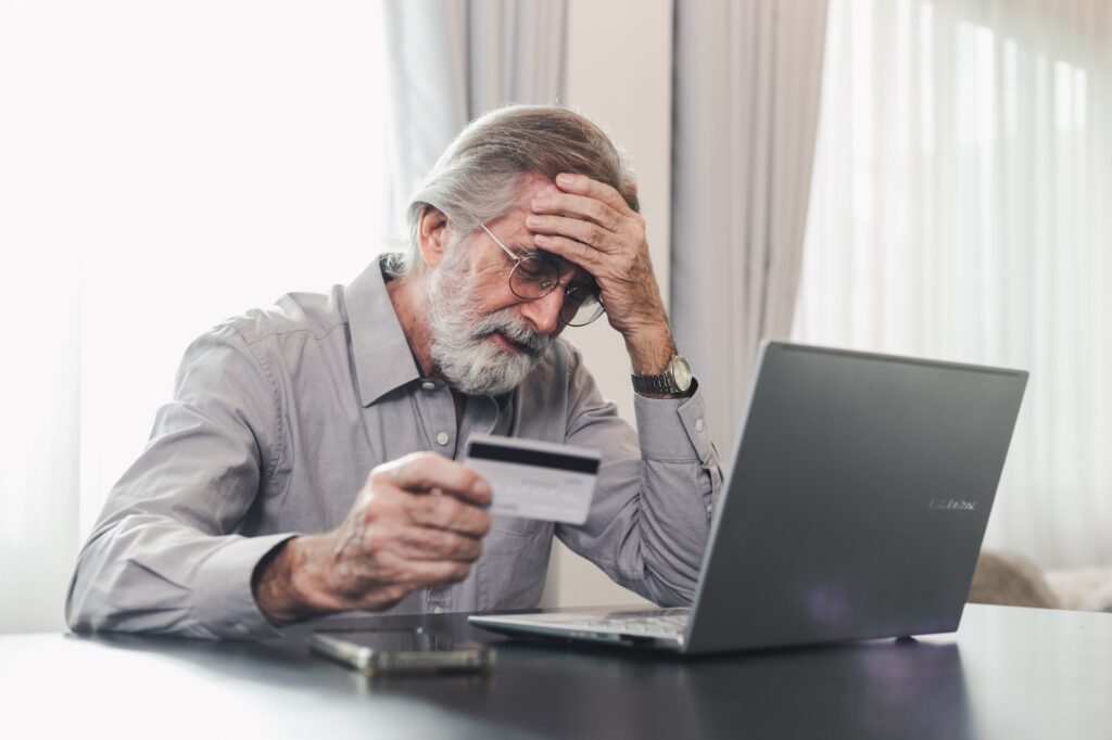 A Ponzi scheme victim looks stressed while reviewing finances and holding a credit card.