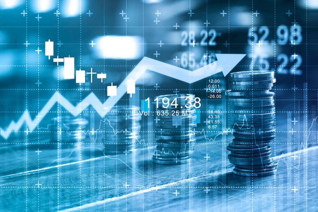 A financial concept with stacks of coins, a graph chart, and candlestick patterns overlaid on a blue-toned digital background, representing market trends, data analytics, and economic growth.